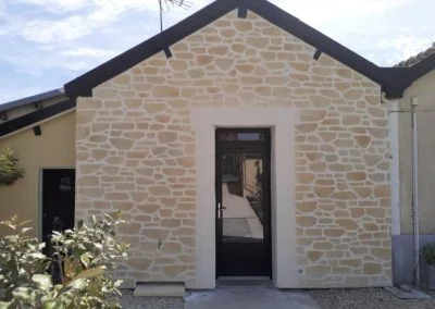 Porte d'entrée vitrée pvc noire sur façade en pierres blanches.